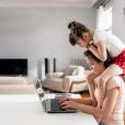 Woman working from home, while her daughter sits on her shoulders