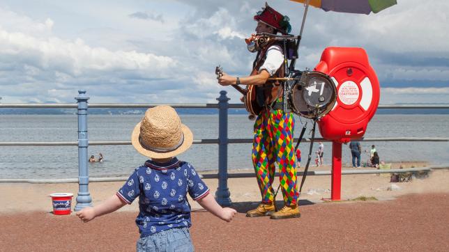Solo baby approaches one-man band on a seafront promenade - independent learners