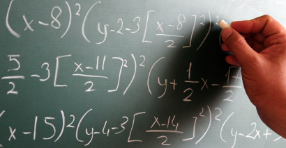 Teacher Writing Algebra & Maths Symbols On Blackboard To Test Students