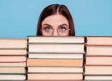 Librarian peers out from behind large pile of books
