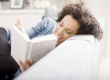 Woman lies on the sofa, reading a book